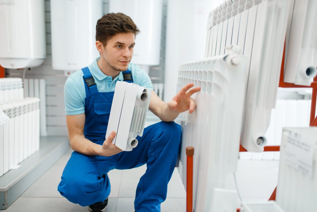 Klempner kniet neben Heizung und hat kleine Heizung in der Hand Die Vorteile der Innungsmitgliedschaft